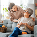 Adult daughter talks and smiles with mother knitting on a couch