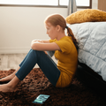 sad girl sitting on the floor at the foot of her bed-min.png