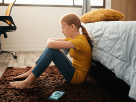 sad girl sitting on the floor at the foot of her bed-min.png