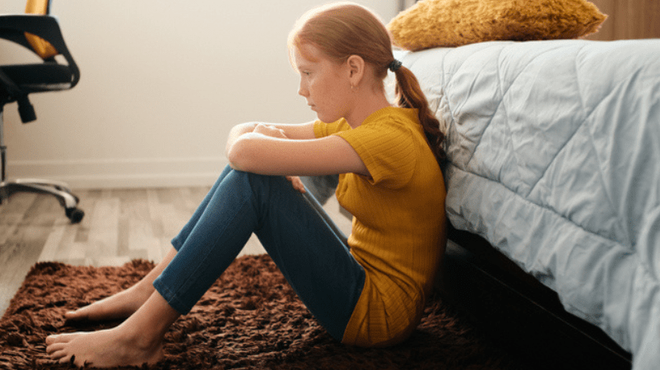 sad girl sitting on the floor at the foot of her bed-min.png