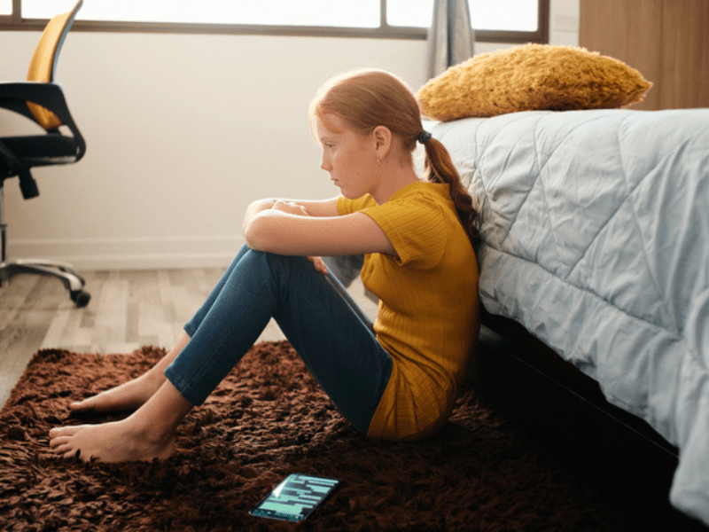 sad girl sitting on the floor at the foot of her bed-min.png