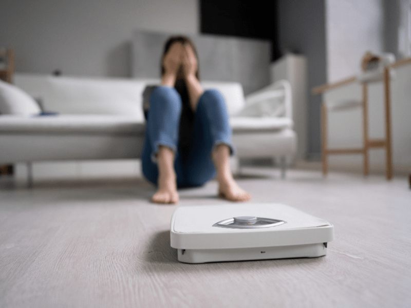 Sad woman sitting next to a scale