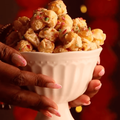 Two hands hold a glass bowl filled with burfee popcorn