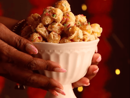 Two hands hold a glass bowl filled with burfee popcorn