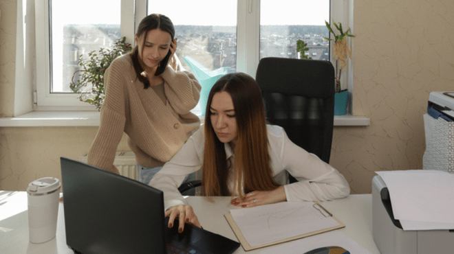 Two women analyse paperwork at an office desk