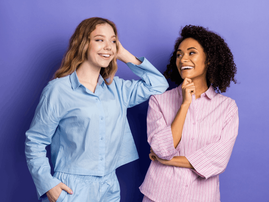 two women wearing pajamas pose against a purple background