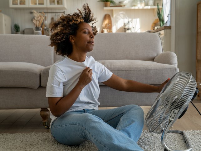 Woman cooling down by ventilator at home