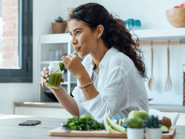 Woman drinks green detox juice in her home kitchen