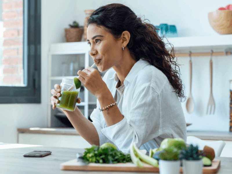 Woman drinks green detox juice in her home kitchen