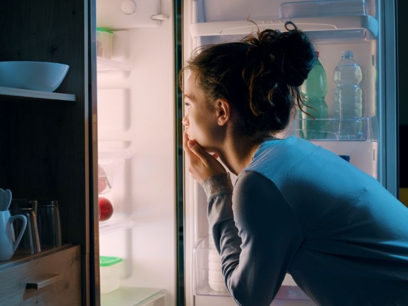 Woman peering into open fridge