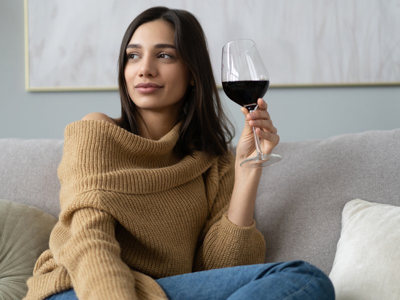 Woman sitting on couch having raised glass with red wine