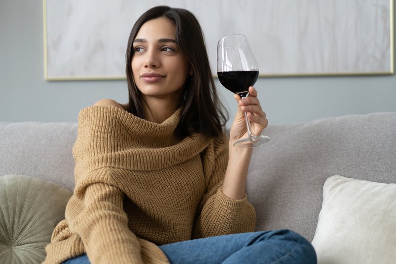 Woman sitting on couch having raised glass with red wine