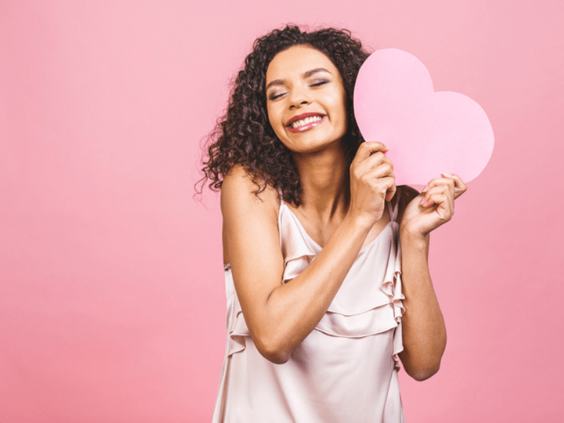 Woman with curly brown hair holding a pink heart
