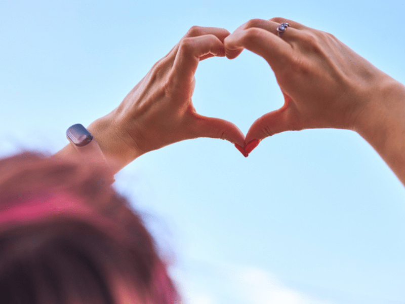 woman with pink hair makes heart gesture with hands