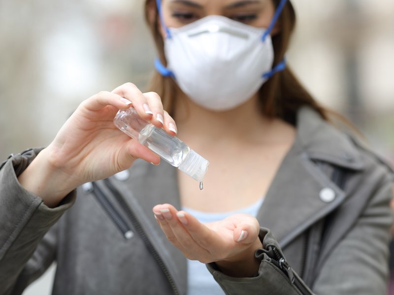 Woman with mask using hand sanitizer preventing contagion