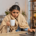 woman working on laptop wrapped in blanket and holding coffee mug