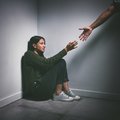 Young woman sitting in the corner of a dark room with a hand reaching out to help her