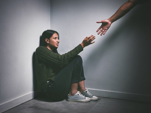 Young woman sitting in the corner of a dark room with a hand reaching out to help her
